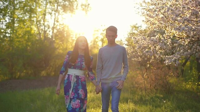 Loving guy and girl in a blooming apple orchard at sunset