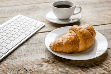 coffee and croissant for breakfast of businessman wooden office desk background