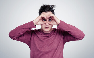 Funny man makes the binoculars around eyes from the hands. On background.