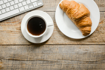 croissant and cup of coffee on office desk for business breakfast wooden background top view mock-up