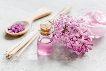 organic salt, cream, extract in lilac cosmetic set with flowers on stone table background