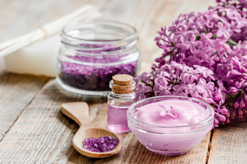 Fototapeta na wymiar organic salt, cream, extract in lilac cosmetic set with flowers on wooden table background