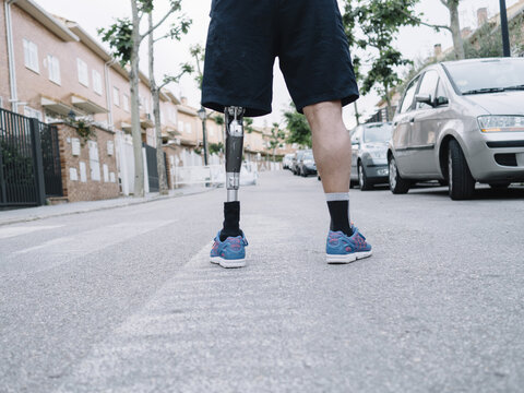Low section of a disable man with prosthesis leg standing on road 