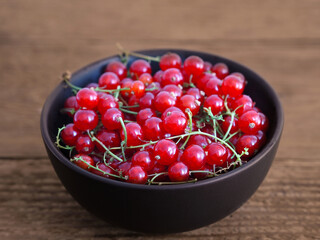 Red currant in black bowl on wooden background