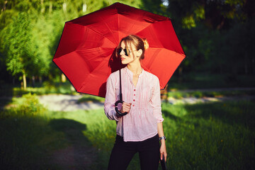 Beautiful young lady holding multicolored umbrella. Blue sky outdoors. Happy girl on countryside landscape