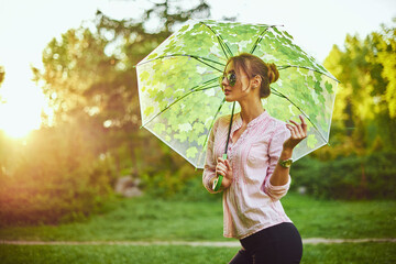 Beautiful young lady holding multicolored umbrella. Blue sky outdoors. Happy girl on countryside...