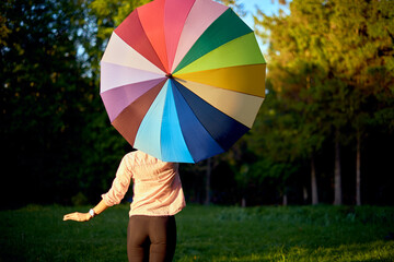 Beautiful young lady holding multicolored umbrella. Blue sky outdoors. Happy girl on countryside landscape