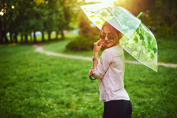 Beautiful young lady holding multicolored umbrella. Blue sky outdoors. Happy girl on countryside...