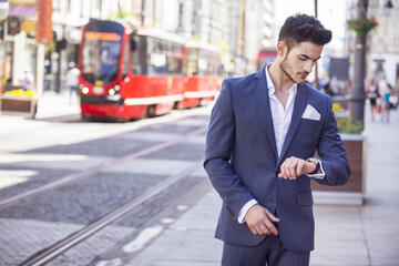Handsome young man elegantly dressed looking at his watch walking through the city