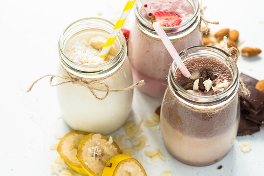 Banana chocolate and strawberry milkshakes in jars on white.