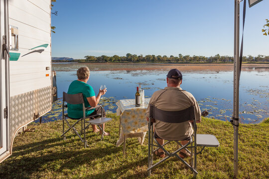 Retired couple sitting outside of caravan with small dog enjoying a wine next to the Lilly filled Lake Kununurra