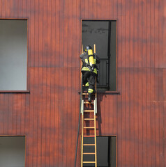Firefighter on the wooden ladder enters the window in the fire s
