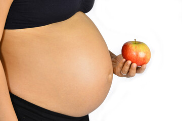 A beautiful pregnant lady holding shiny apple in front of her glowing pregnancy bump.