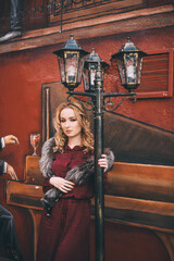 Naklejka na ściany i meble Молодая красивая девушка в бордовом платье и меховом воротнике стоит под фонарем на фоне граффити 
