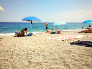 close up of beach sand with blurry people relaxing by the sea in the background