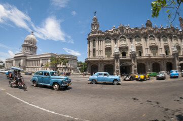 Fototapeta na wymiar Bright wide-angle view of the daily life on one of the main streets in central Havana, Cuba with classic taxi cars passing the Capitolio and Gran Teatro de La Habana landmarks