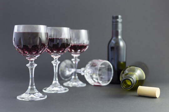 Concept of alcohol consumption, alcoholism and abuse with a line of beautiful crystal glasses filled with red wine, a full and an empty bottle. Stages of drinking underlined by blurred image effect.