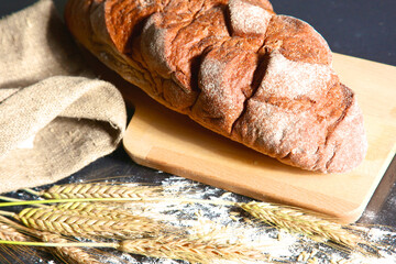 rustic crusty bread and wheat ears on a dark wooden table
