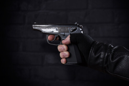 Gangster with a gun in his hand and a leather jacket on a dark background