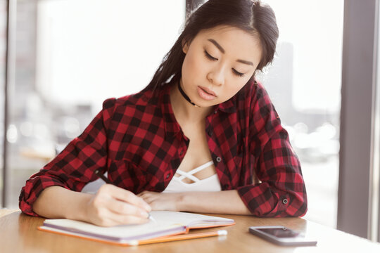 attractive asian student writing in diary and sitting in cafe