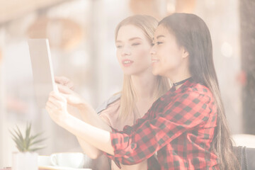 Smiling young women drinking coffee and using digital tablet together, coffee break concept