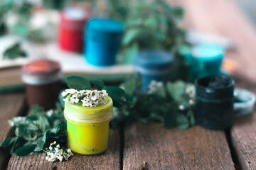 Jar of paint on a wooden background with leaves of plants.