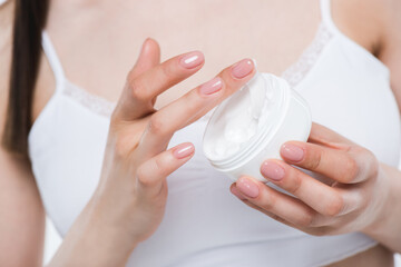 Close-up partial view of young woman in underwear holding container with body cream