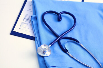 Medical stethoscope twisted in heart shape lying on patient medical history list and blue doctor uniform closeup