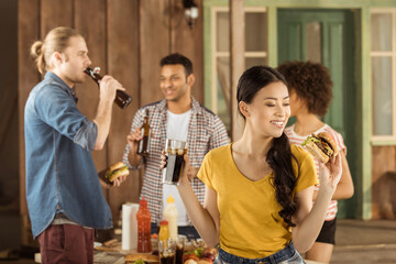 young asian girl eating burger and drinking cola with friends at picnic on patio