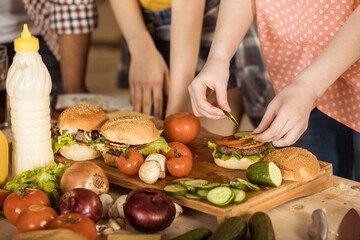 cropped shot of woman preparing tasty hamburgers for friends on kitchen board