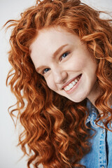 Close up of redhead beautiful girl with freckles smiling looking at camera over white background.