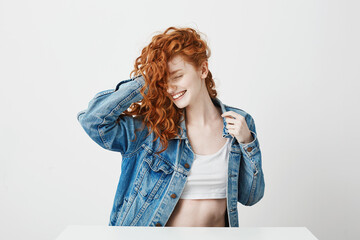 Happy beautiful girl smiling with closed eyes touching her red curly hair over white background.