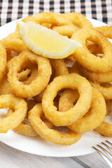 Close-up of platter of squid to la romana and a lemon on white wooden table. Squids. Vertical shoot.