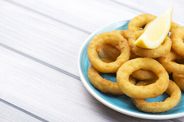 Plate of squid a la romana and a lemon on white wooden table. Squids. Horizontal shoot....