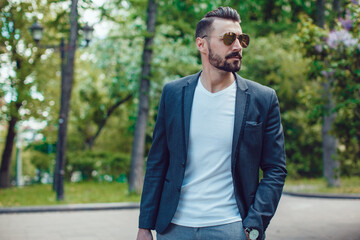 Fototapeta premium Stylish man with a beard and in sunglasses standing in the park.
