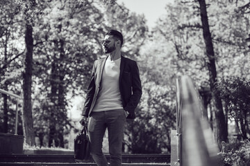 Fototapeta premium A stylish man with a beard and wearing sunglasses goes down the stairs in the street.