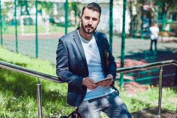 Stylish man with a beard and in sunglasses stands on the street and uses a tablet.