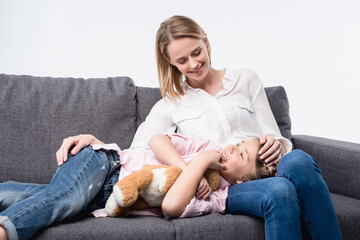 Obraz premium smiling mother with little daughter sitting on sofa together isolated on white