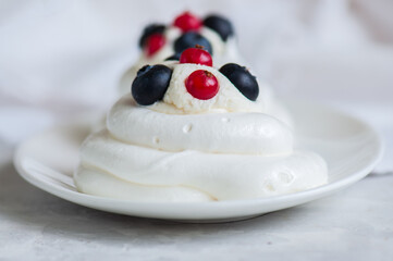 Close up of homemade individual meringue cakes Pavlova with whipped cream with mascarpone fresh blueberries and red currants in a white plate on a white stone background.