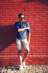 Young man wearing a blue shirt and torn shorts against a brick wall