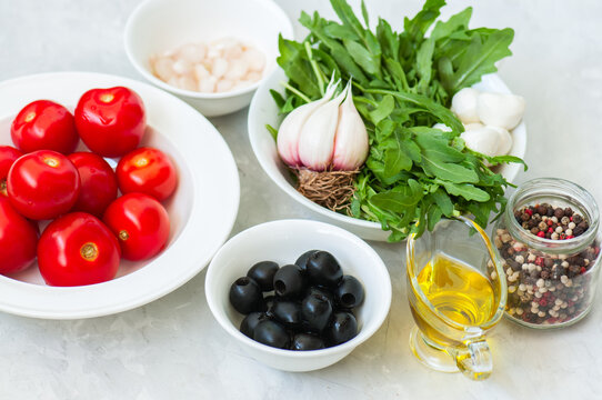 Ingredients for healthy salad. Tomatoes, rucola, onion, mozzarella, olives, garlic and pepper with olive oil on a white stone background.