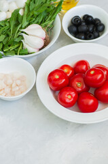 Ingredients for healthy salad. Tomatoes, rucola, onion, mozzarella, olives, garlic and pepper with olive oil on a white stone background.