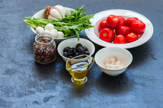 Ingredients for healthy salad. Tomatoes, rucola, spring onion, mozzarella, olives, garlic and pepper with olive oil on a black slate background.
