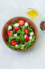Close up of fresh salad with rucola, tomatoes  olives, onion, mozzarella and spices in a bowl on a white stone background with copy space. Healthy food, Diet, Detox, Clean Eating or Vegetarian concept