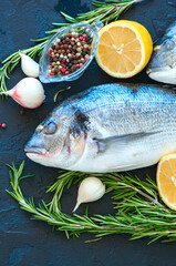 Close up of fresh raw dorado fish, rosemary herb garlic pepper and half of lemon on a black slate background. Overhead view.