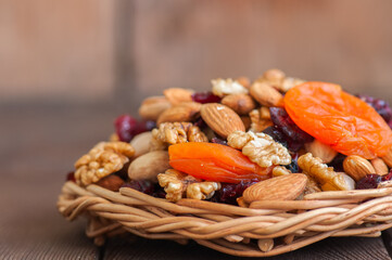 Mix of nuts and dry fruits in a wooden plate. Assortment of walnuts, almonds, roasted cashews, pistachios, dry apricots, cranberries and raisins. Copy space and selective focus.