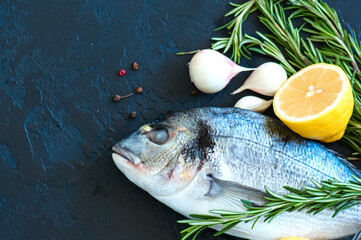 Close up of fresh raw dorado fish, rosemary herb garlic pepper and half of lemon on a black slate background. Overhead view.