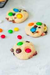 Cookies with colorful candies and chocolate chips on a white stone background.