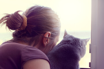 spending time together/ Girl with a cat looking at the street in an open window