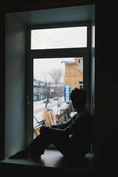 a man sitting on the window and looking outside 